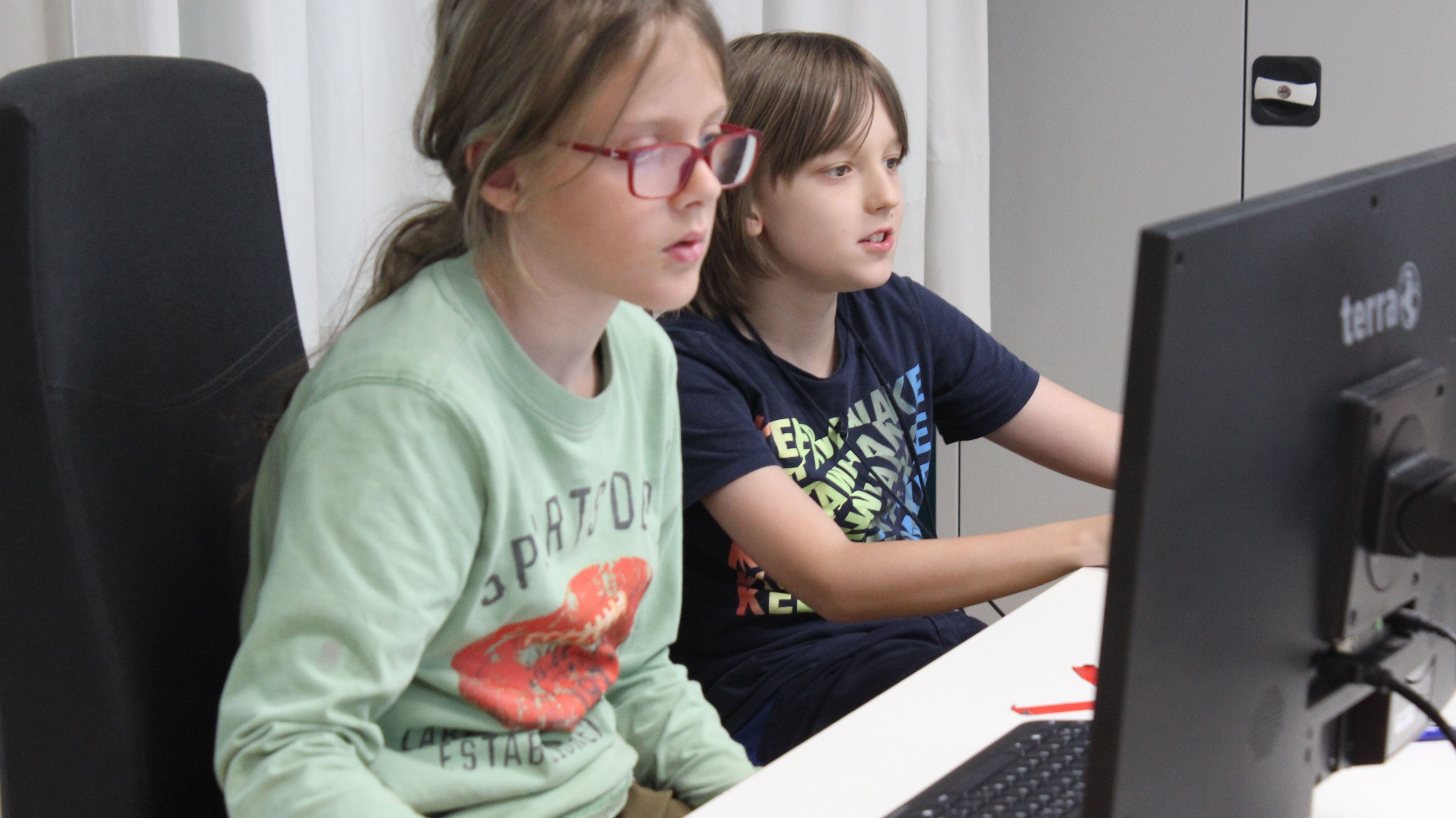 Zwei Kinder arbeiten an einem Computer mit Bildschirm und Tastatur