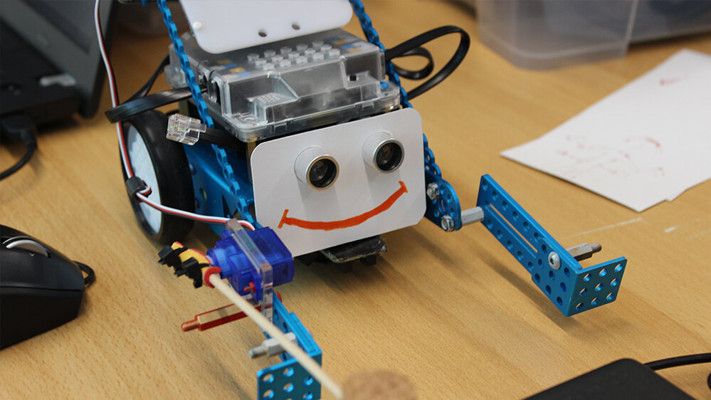 Roboter in blau mit einem lächelnden Mund und Armen aus Metall steht auf einem Tisch