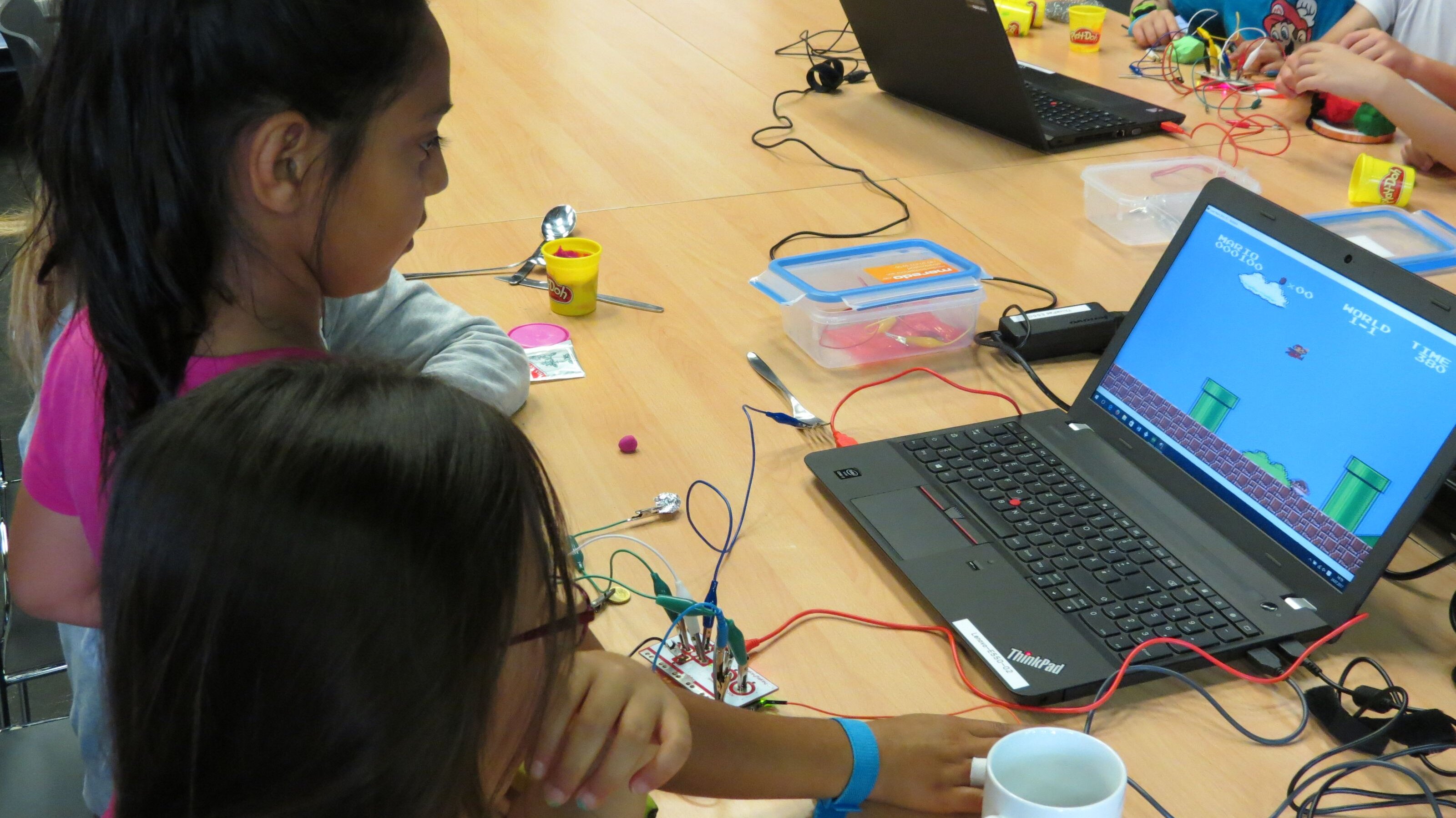 zwei Mädchen bedienen den Computer mit einer Makey Makey Platine