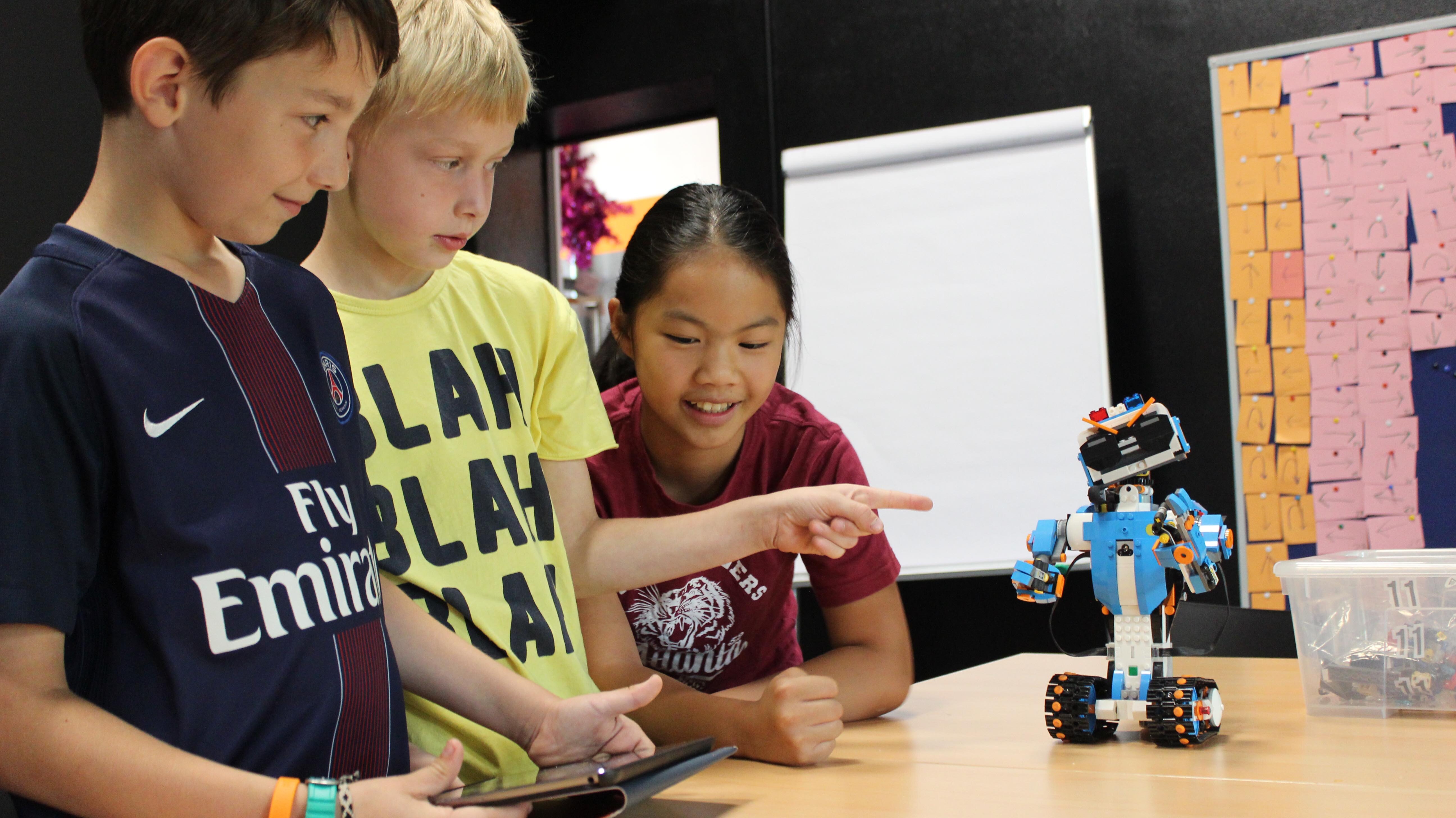 Drei Kinder programmieren einen Roboter mit dem Tablet.