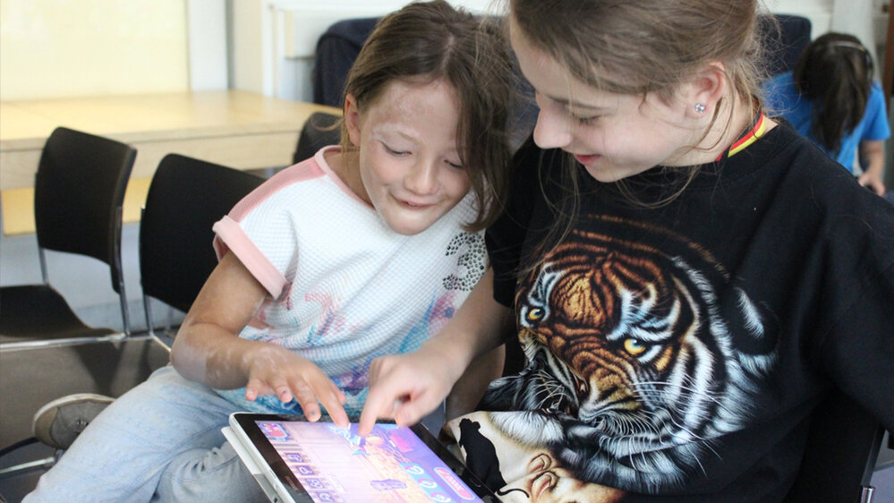 Zwei Mädchen spielen zusammen ein Spiel an einem Tablet.