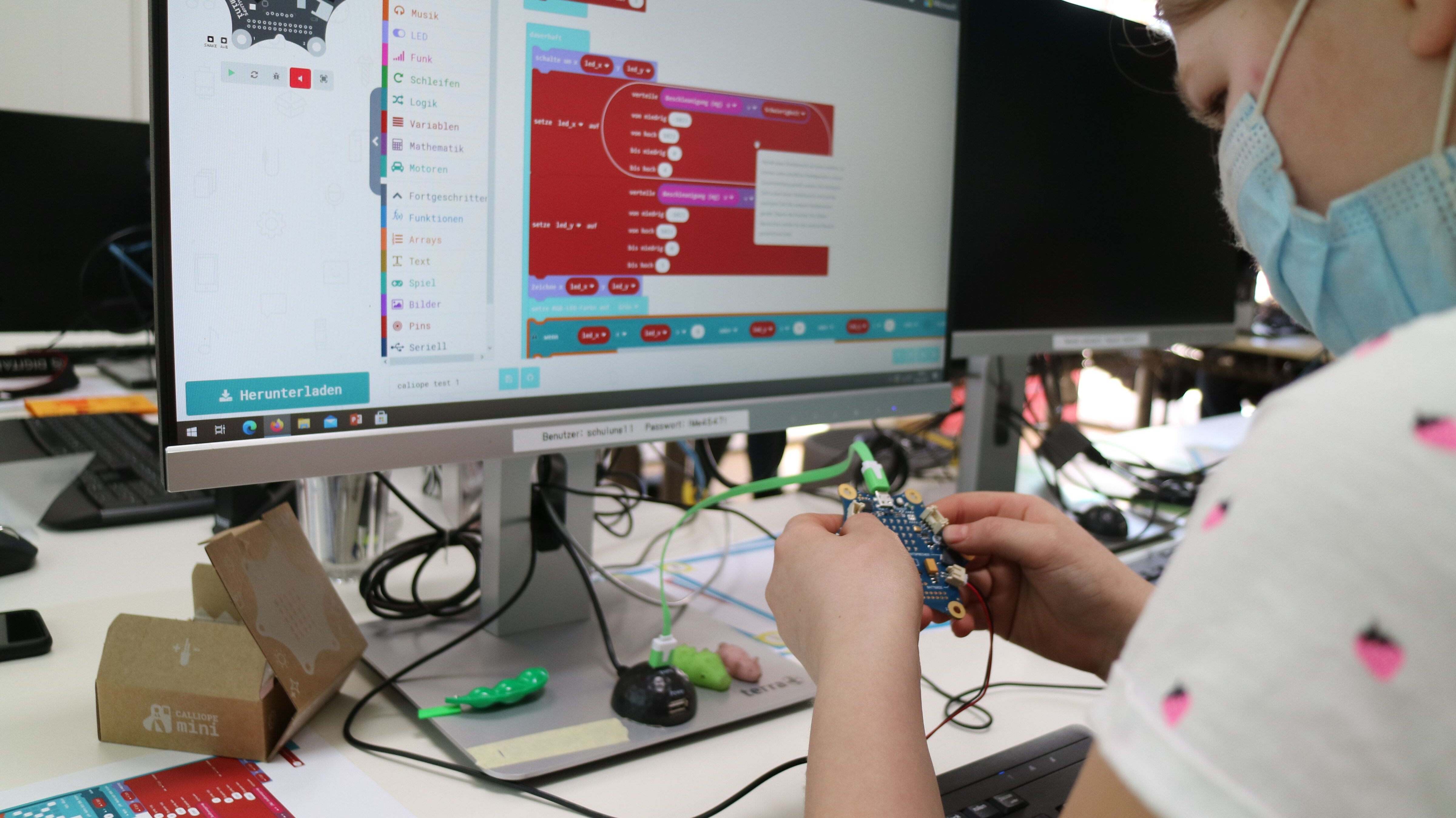 Mädchen arbeitet am Calliope vor einem Computer, auf dem man eine Programmierung sieht
