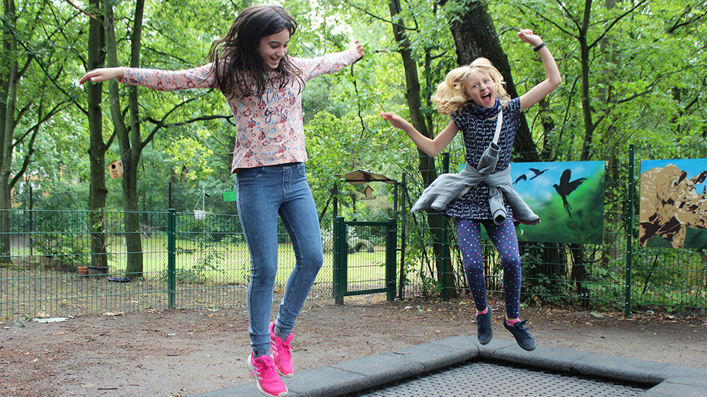 zwei Mädchen springen auf einem Bodentrampolin und lachen