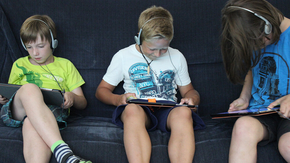 Drei Jungen spielen ein Spiel an ihren Tablets.