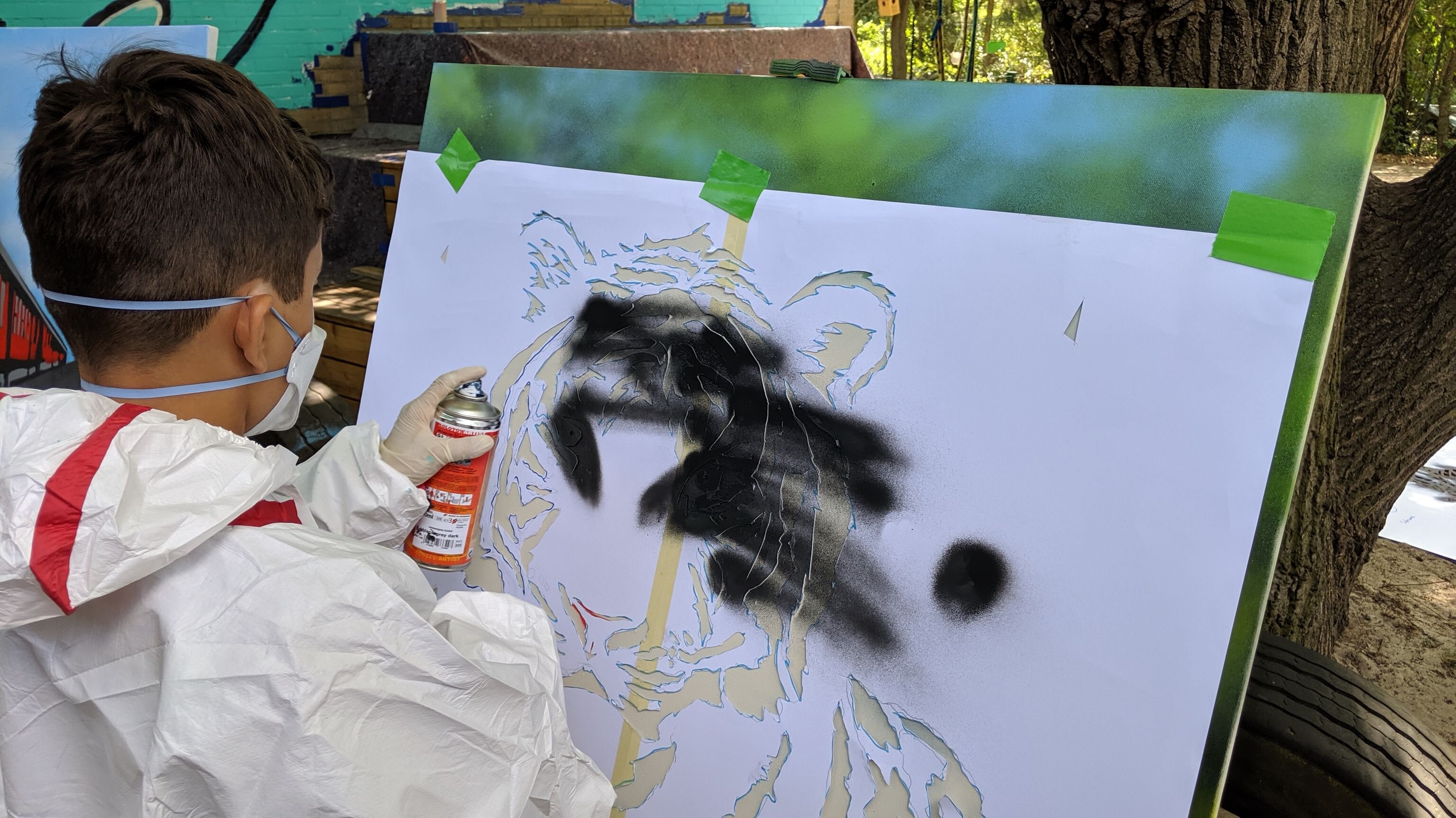 Junge sprüht Farbe auf eine Leinwand mit Schablone