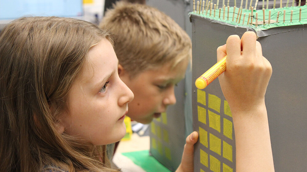 Mädchen malt Fenster auf ein 3D Hochhaus-Modell