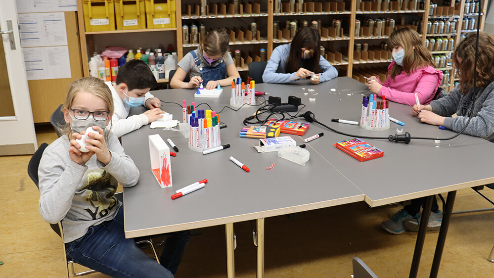 Kinder sitzen am Tisch und bearbeiten 3D-Figuren