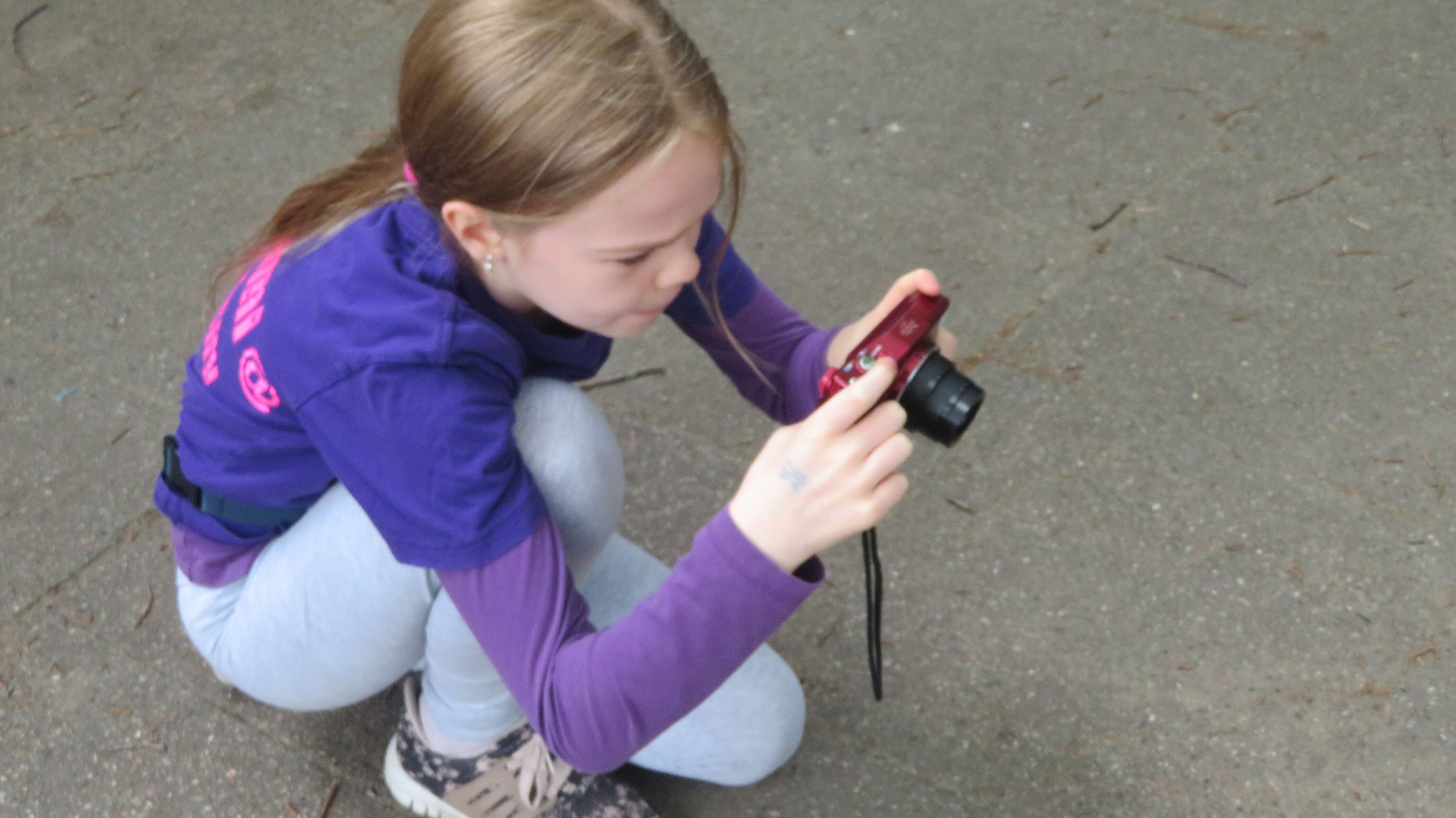 Mädchen hockt auf dem Boden und fotografiert mit einer Kompaktkamera