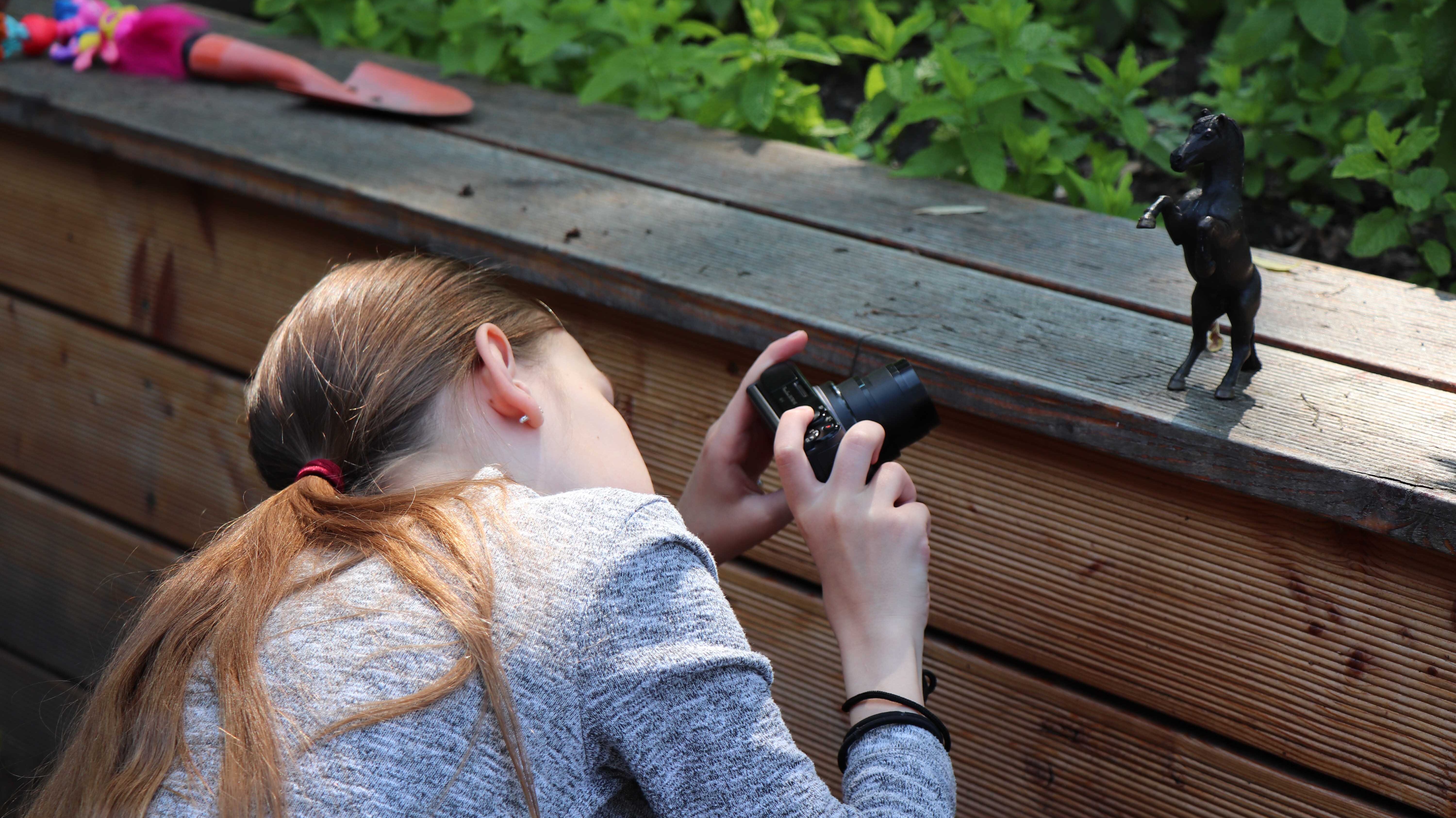 Mädchen hockt und fotografiert eine Figur auf einer Bank