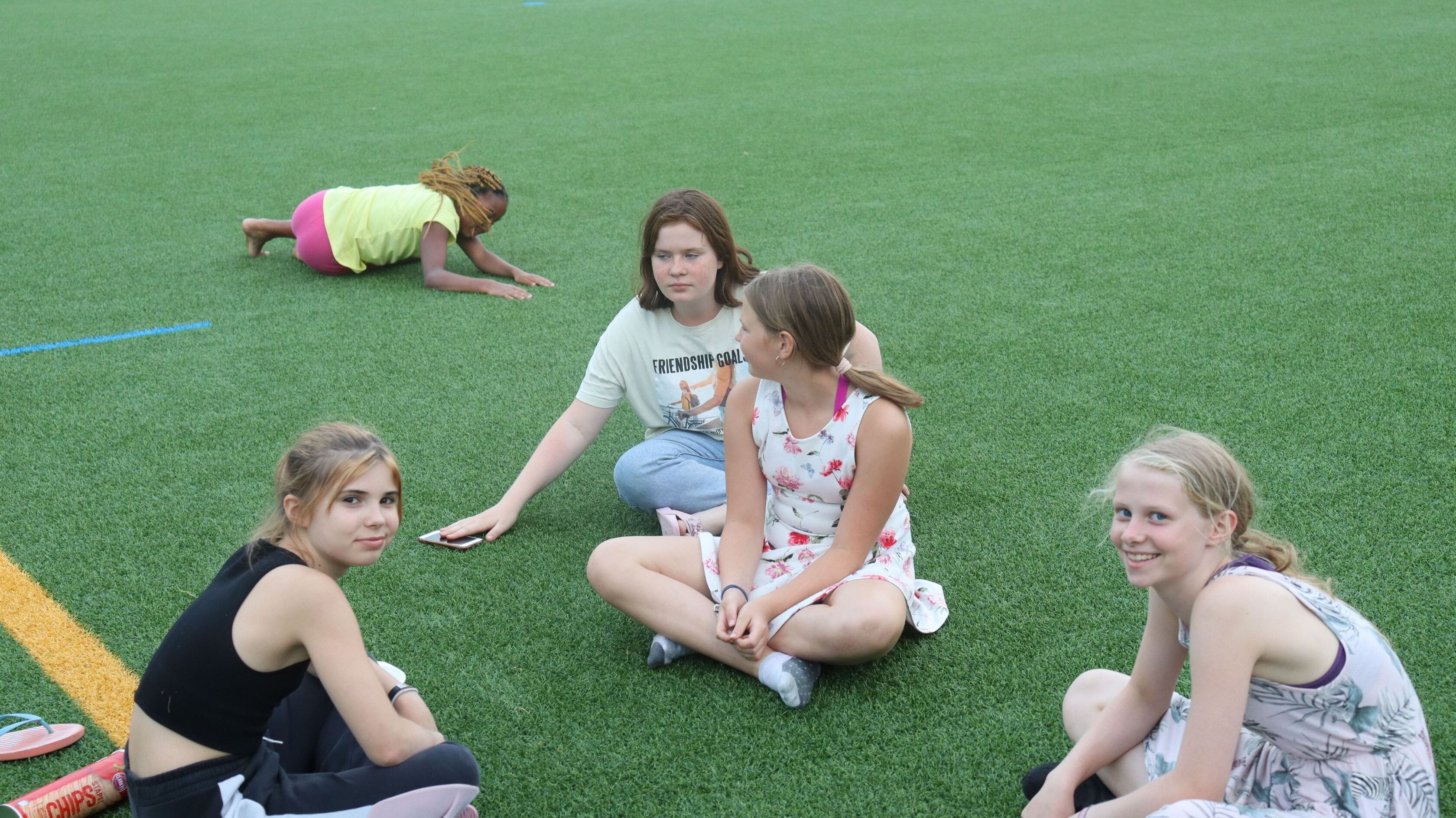 Mädchen sitzen auf einer Kunstrasenfläche