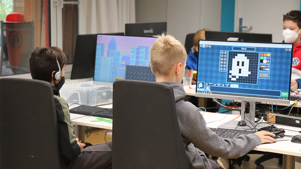 Zwei Jungen sitzen vor je einem Computer und arbeiten an einem Programm