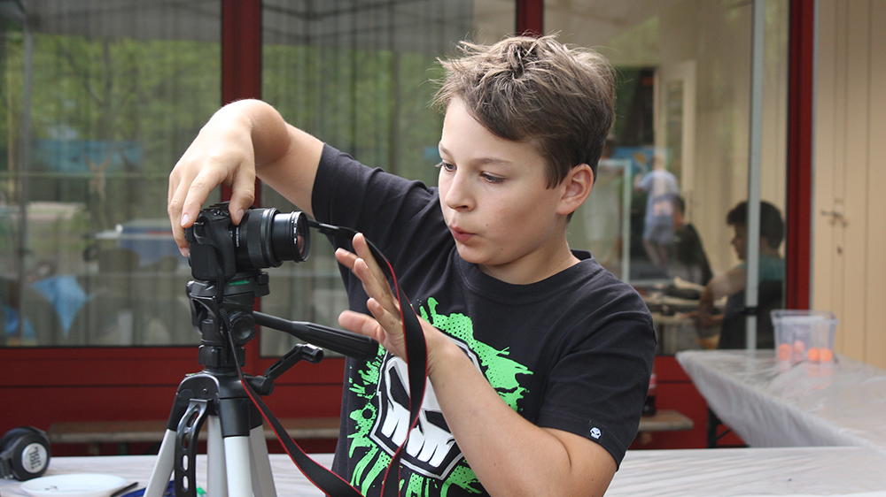 Ein Junge schraubt eine Kamera auf ein Stativ