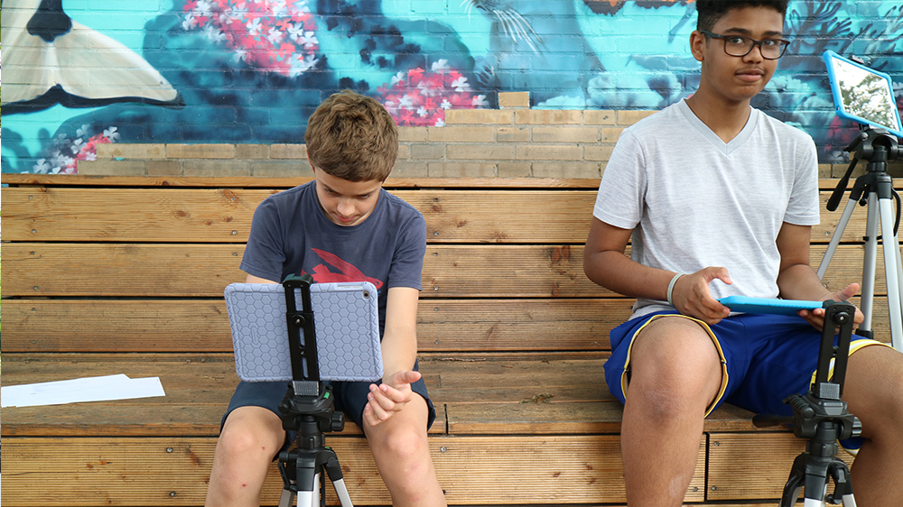 Zwei Jungen sitzen nebeneinander vor zwei iPads auf Stativen