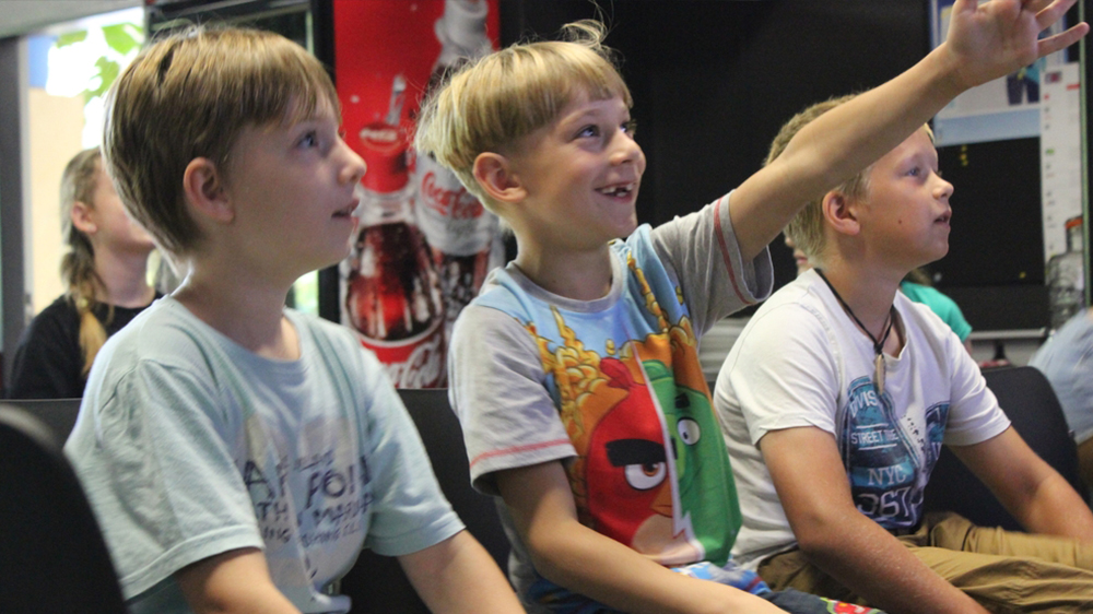 Drei Kinder sitzen nebeneinander und freuen sich über etwas