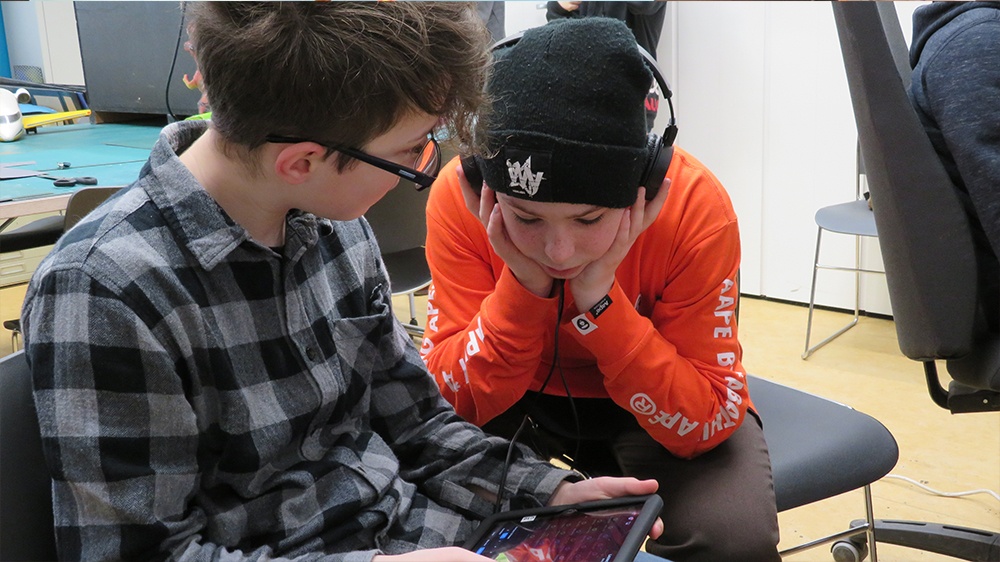 Zwei Jungen sitzen vor einem Tablet mit Kopfhörern