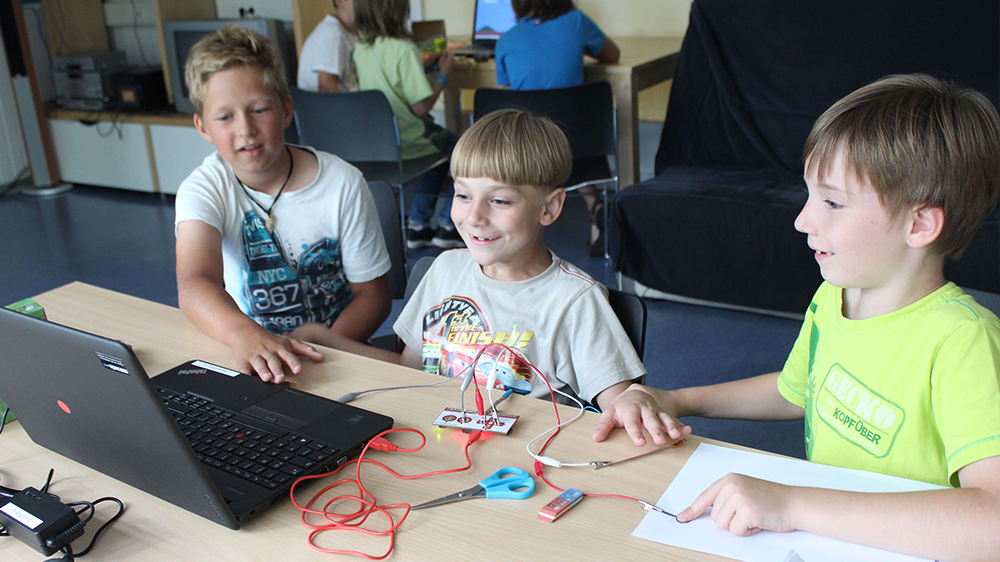 Drei Jungen spielen mit Makey Makey am Laptop.