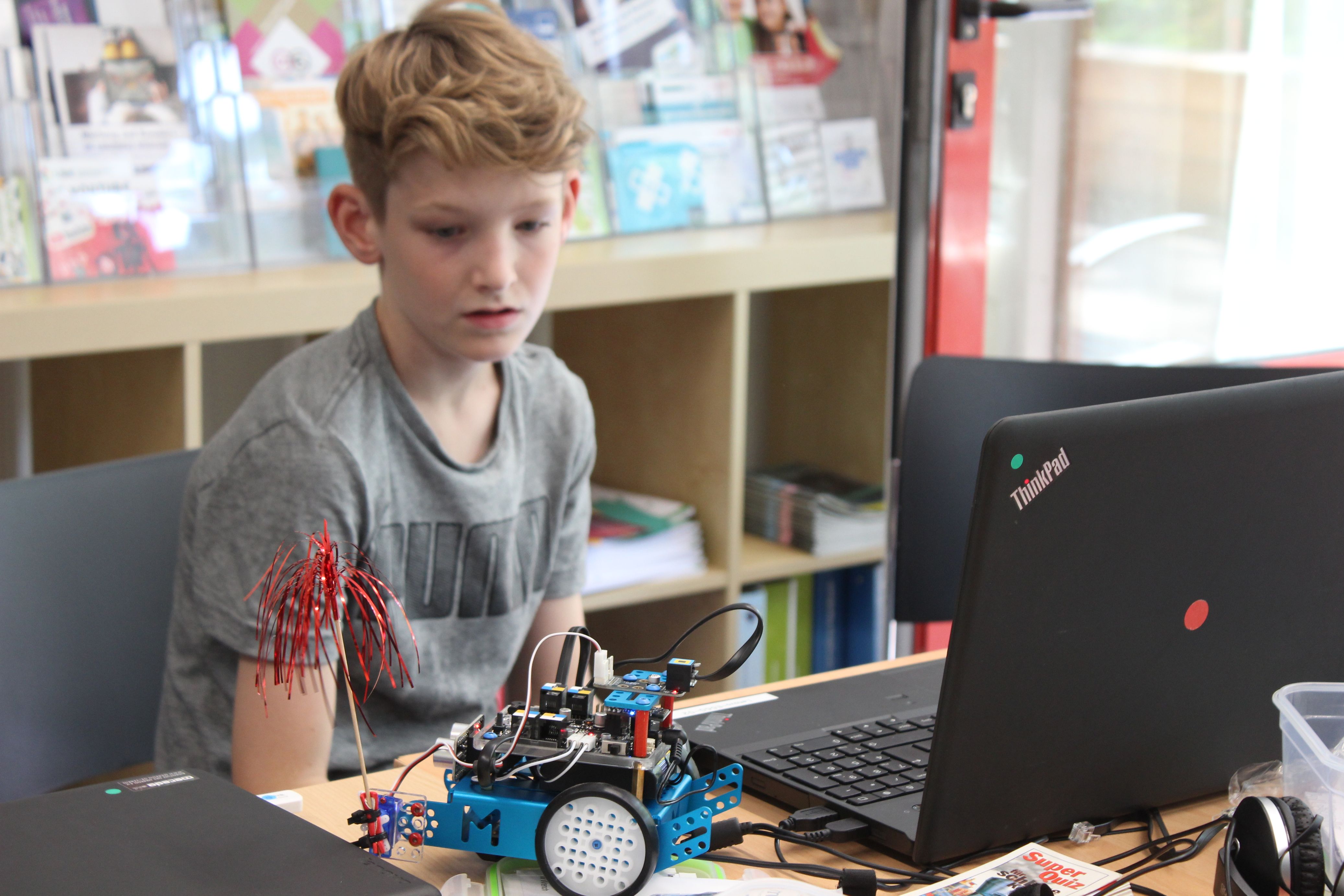 Junge schaut auf einen blauen Roboter neben einem Laptop
