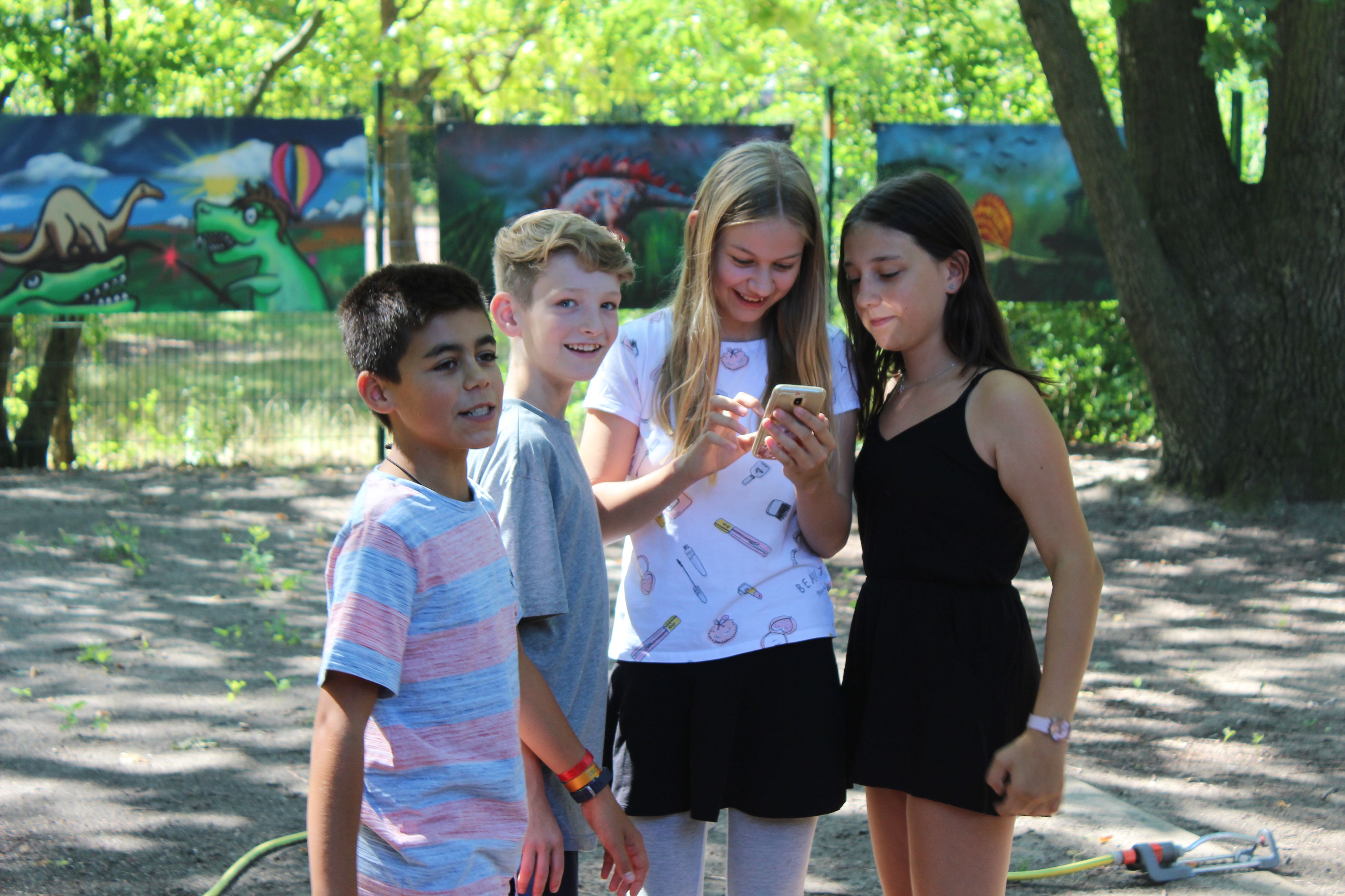 Vier Kinder stehen draußen und schauen sich etwas auf einem Handy an