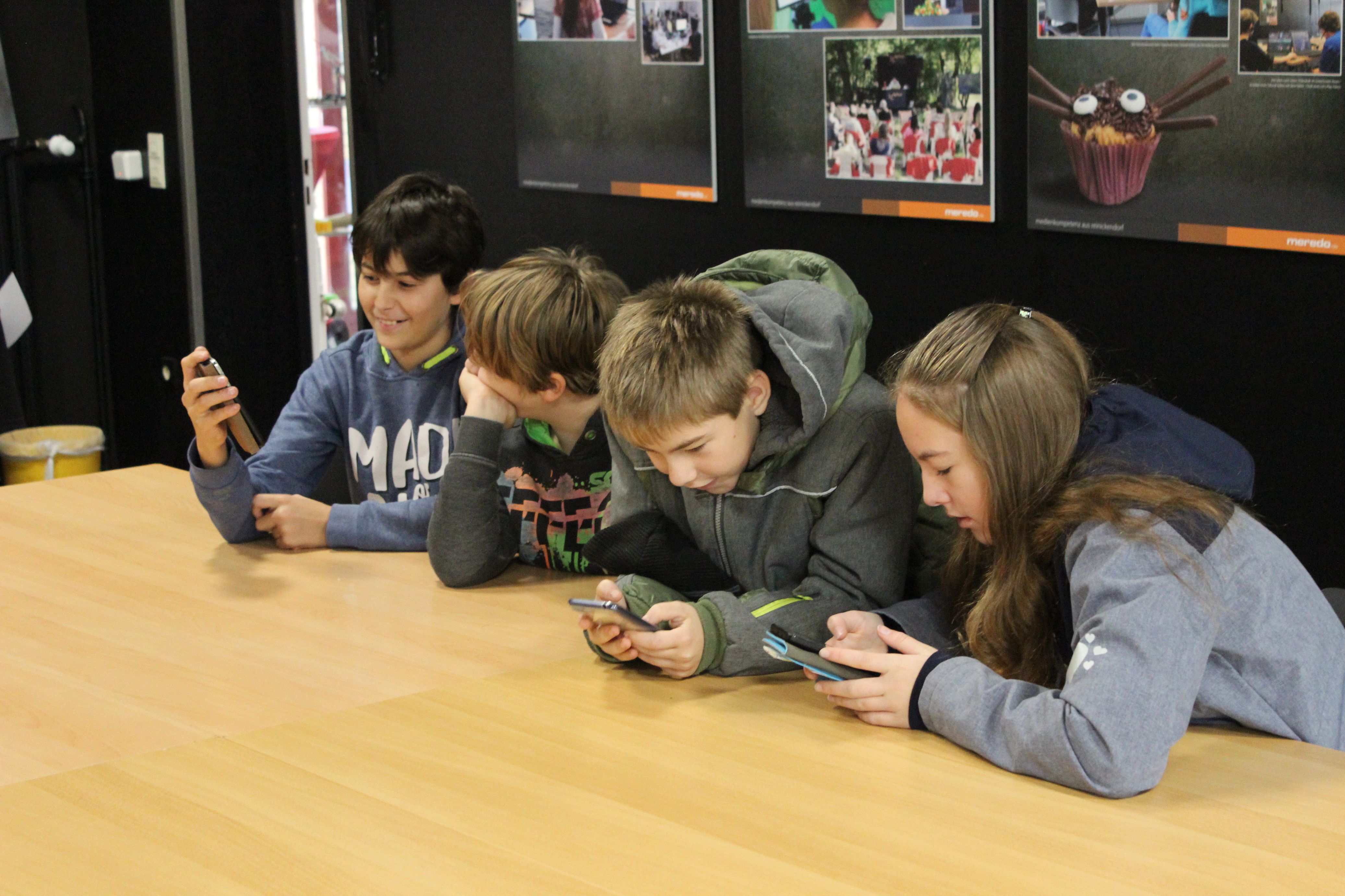Vier Schüler sitzen an einem Tisch und schauen auf Handys