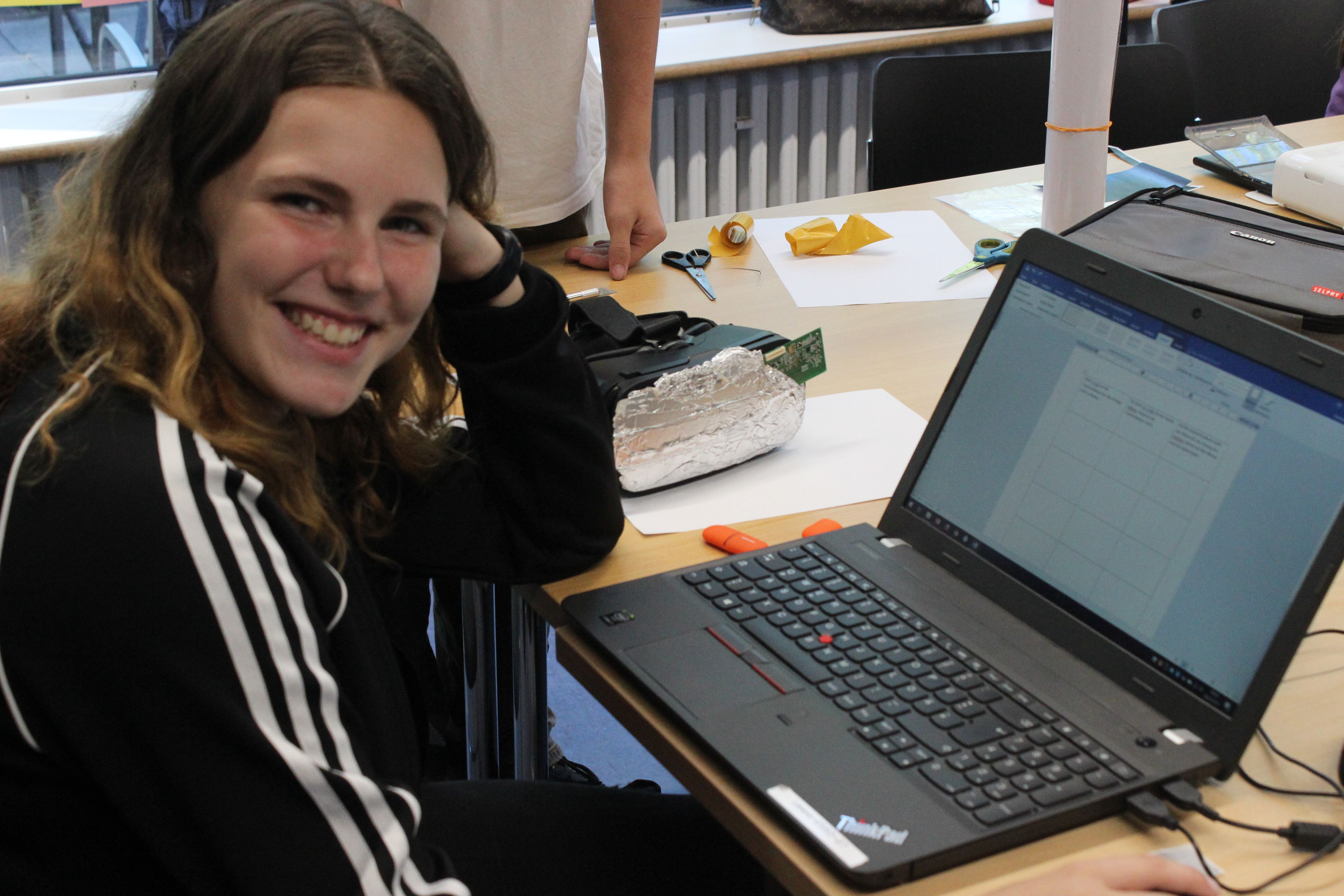 Schülerin sitzt an einem Laptop und lächelt